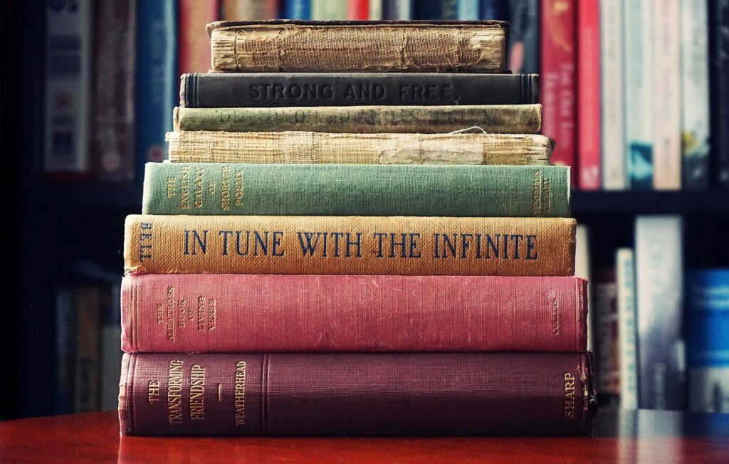 A stack of vintage hardcover books on a wooden table in a cozy library setting.